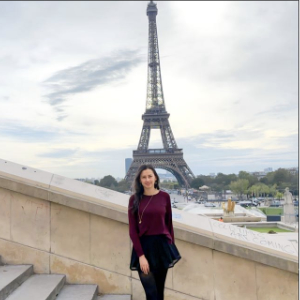Mujer parada frente a la torre Eiffel en un día nublado.